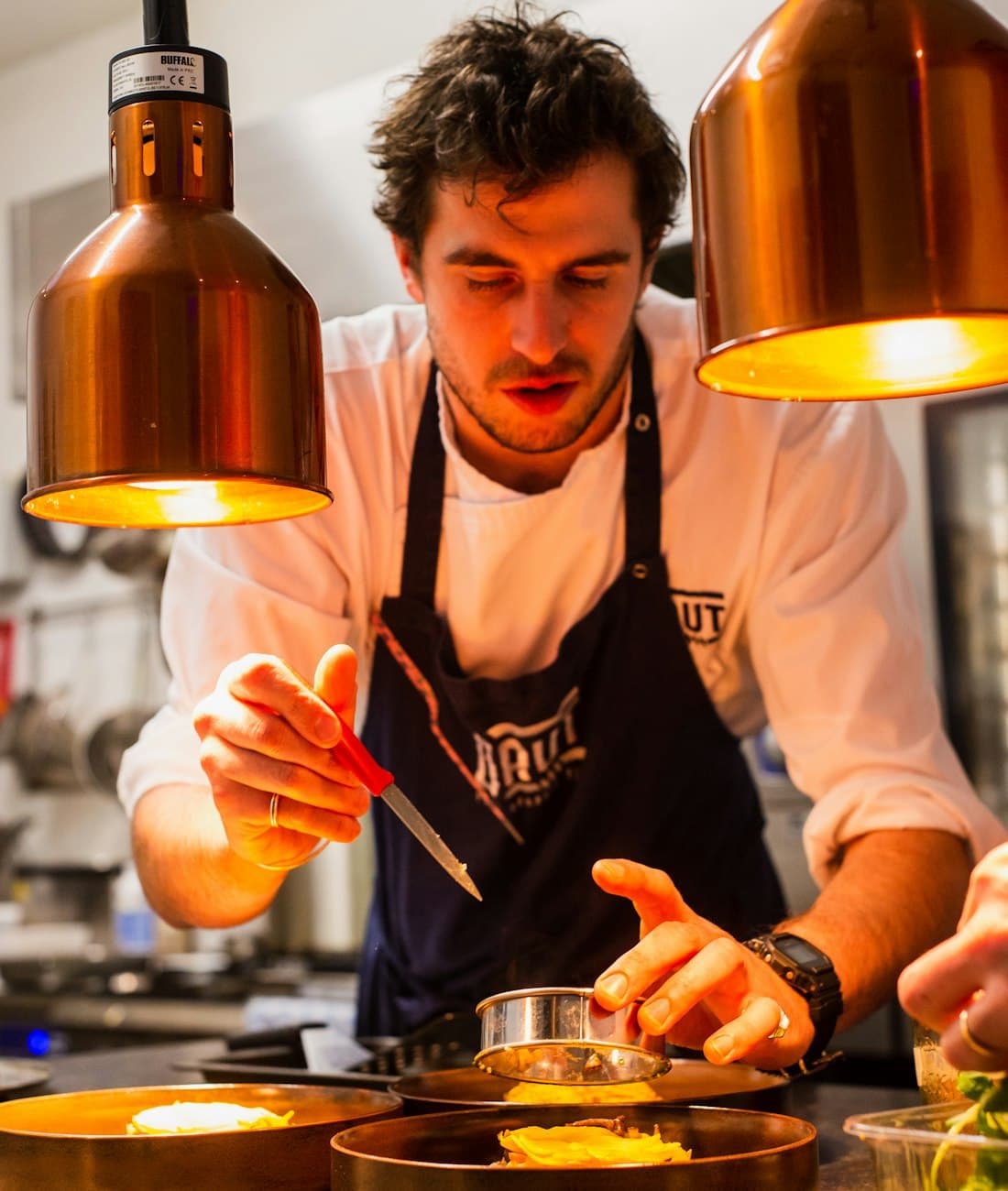 Chef plating a dish under the heat lamps